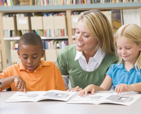 Two students in class reading with teacher